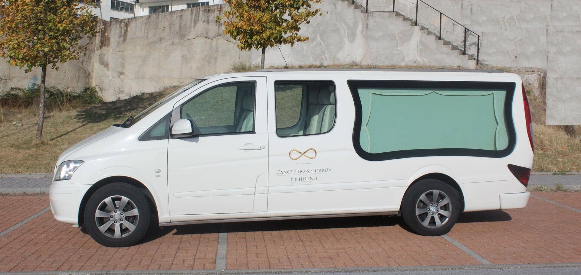 Carro funerário branco estacionado sobre tijolos.