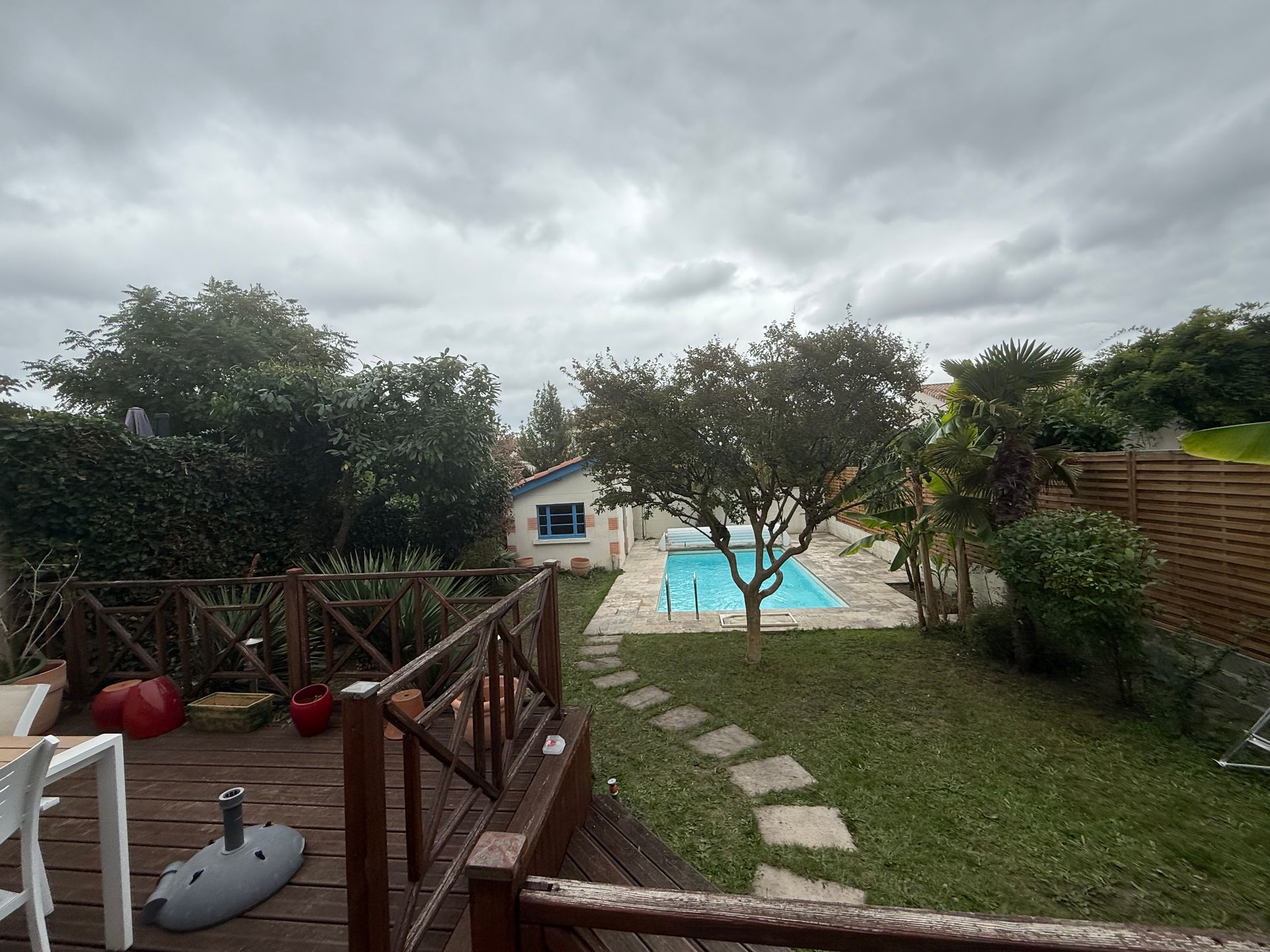 Cour arrière avec piscine, petits arbres, allée gazonnée et ciel nuageux.