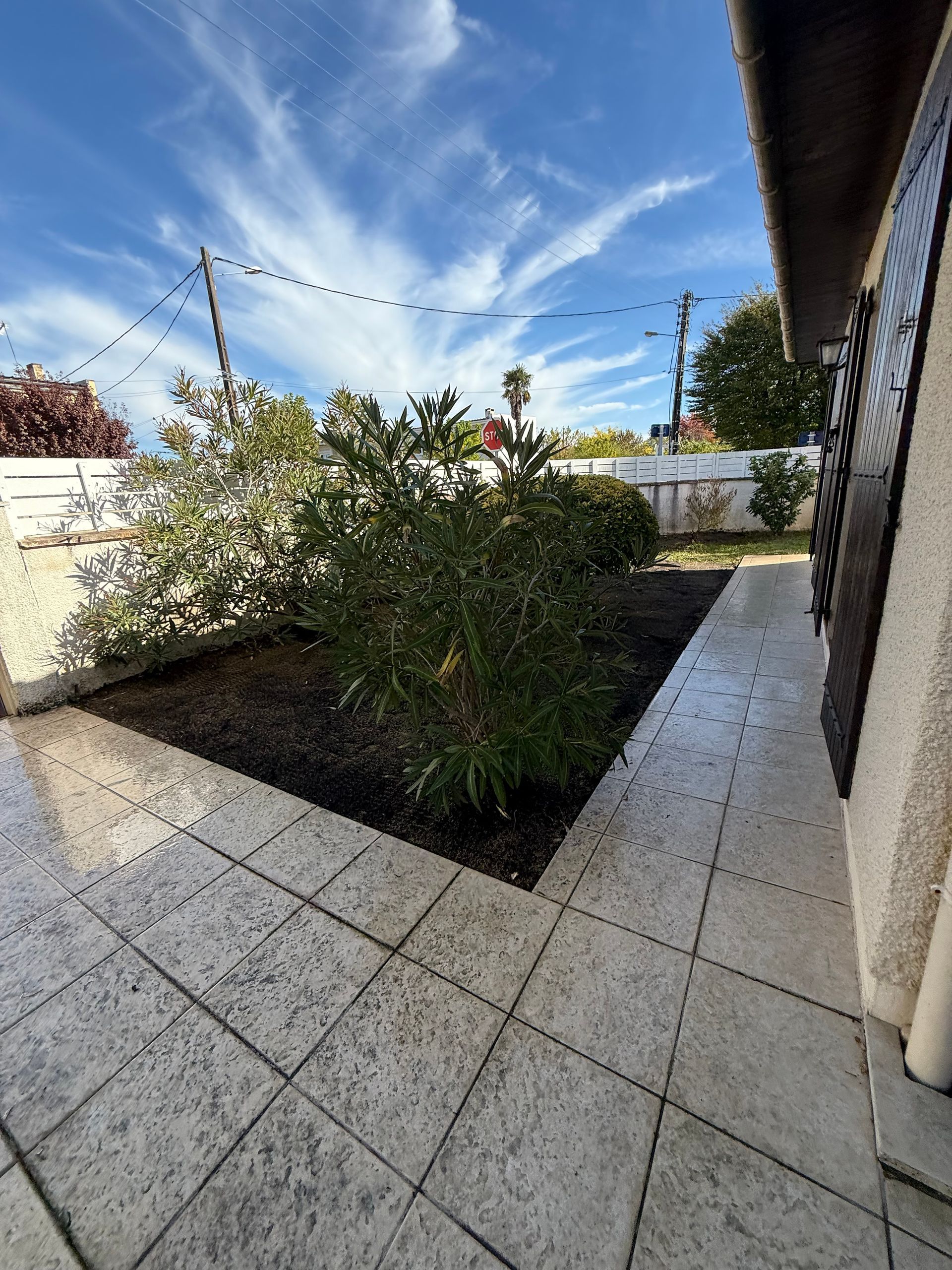 Un patio avec des carreaux carrés à côté d'un parterre de buissons verts contre un ciel bleu vif.