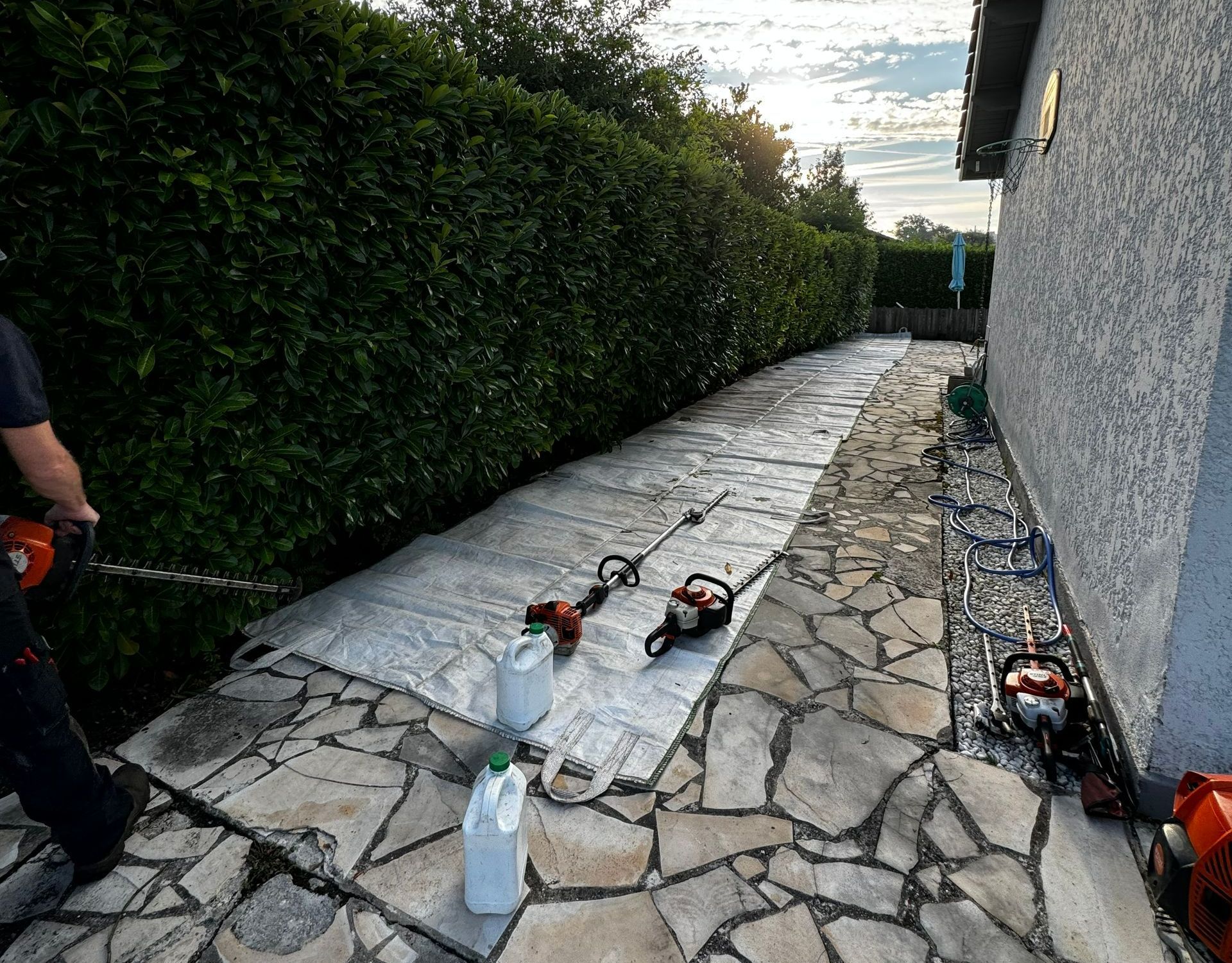 Une personne avec un taille-haie devant une grande bâche le long de la haie.