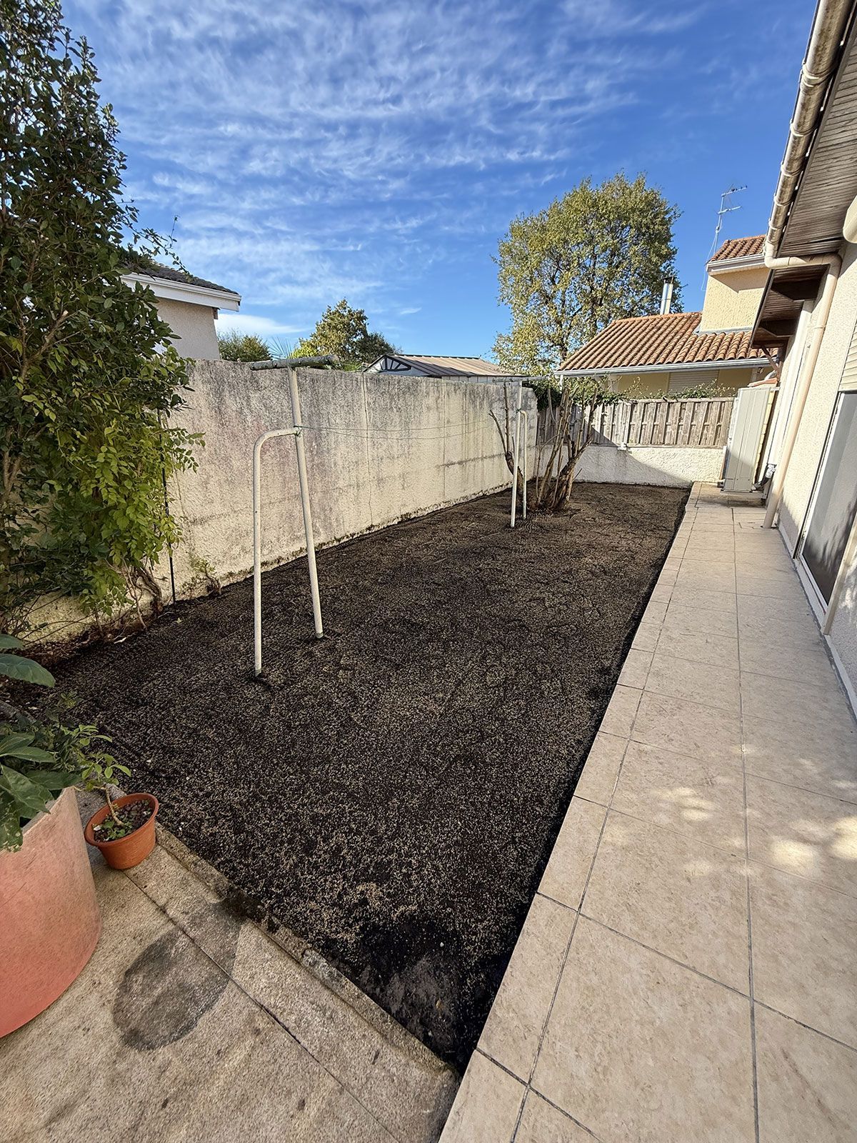 Arrière-cour avec sol foncé, murs blancs, cordes à linge et un chemin sous un ciel bleu.