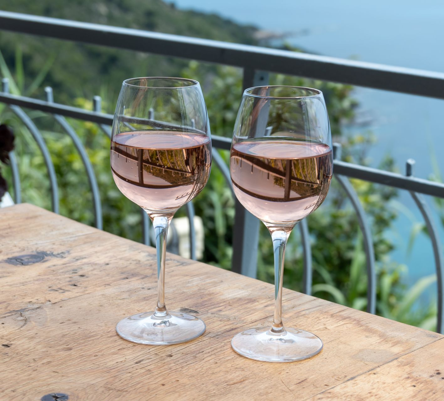 Deux verres de rosé sur une table en bois donnant sur un lac pittoresque et une balustrade à flanc de colline.