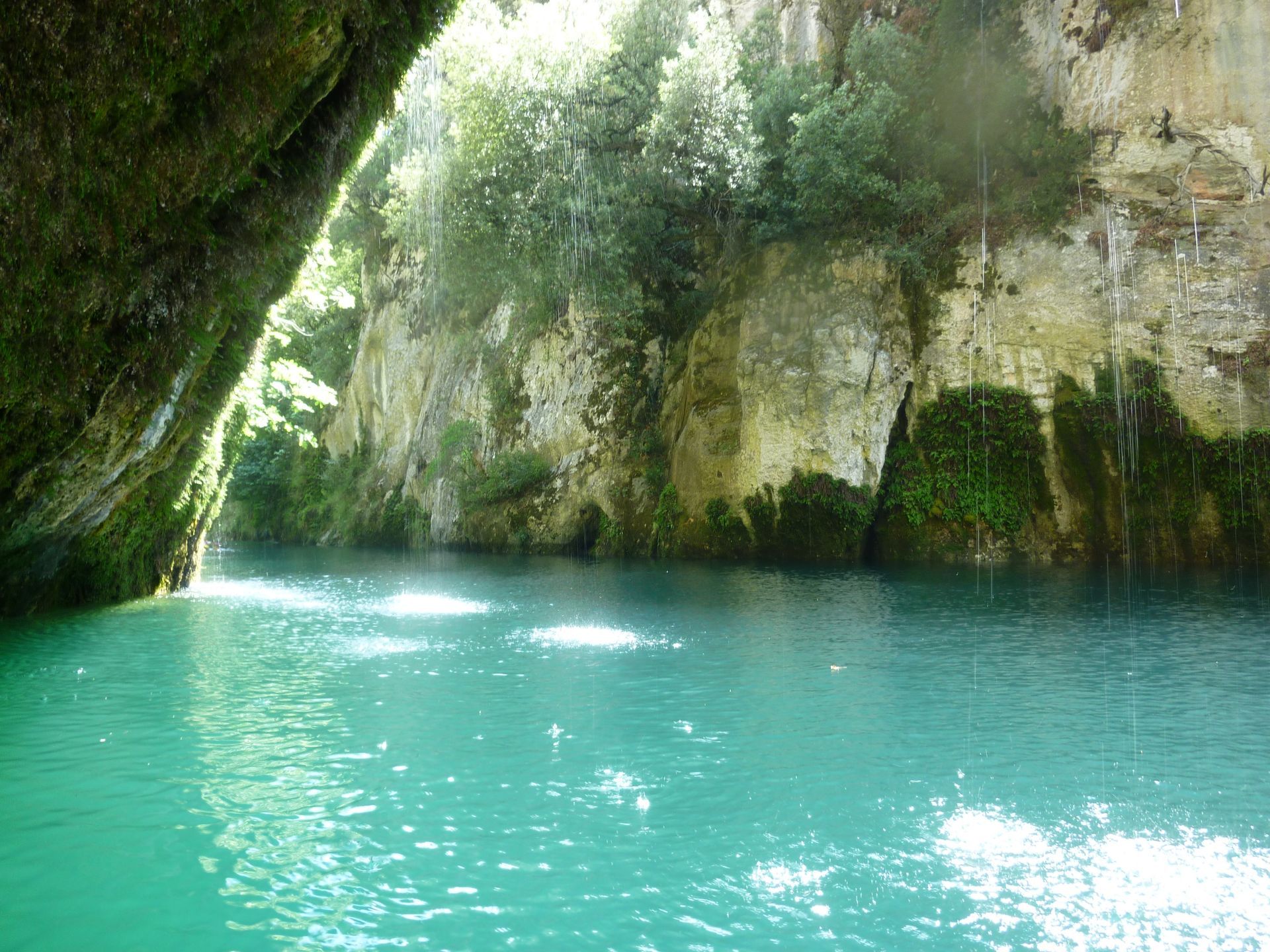 Lagon au pied d'une grotte rocheuse, où le soleil se reflète sur l'eau et la végétation luxuriante.