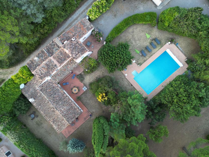 Vue aérienne d'une maison au toit de tuiles, bordée d'une piscine et entourée d'une végétation luxuriante.