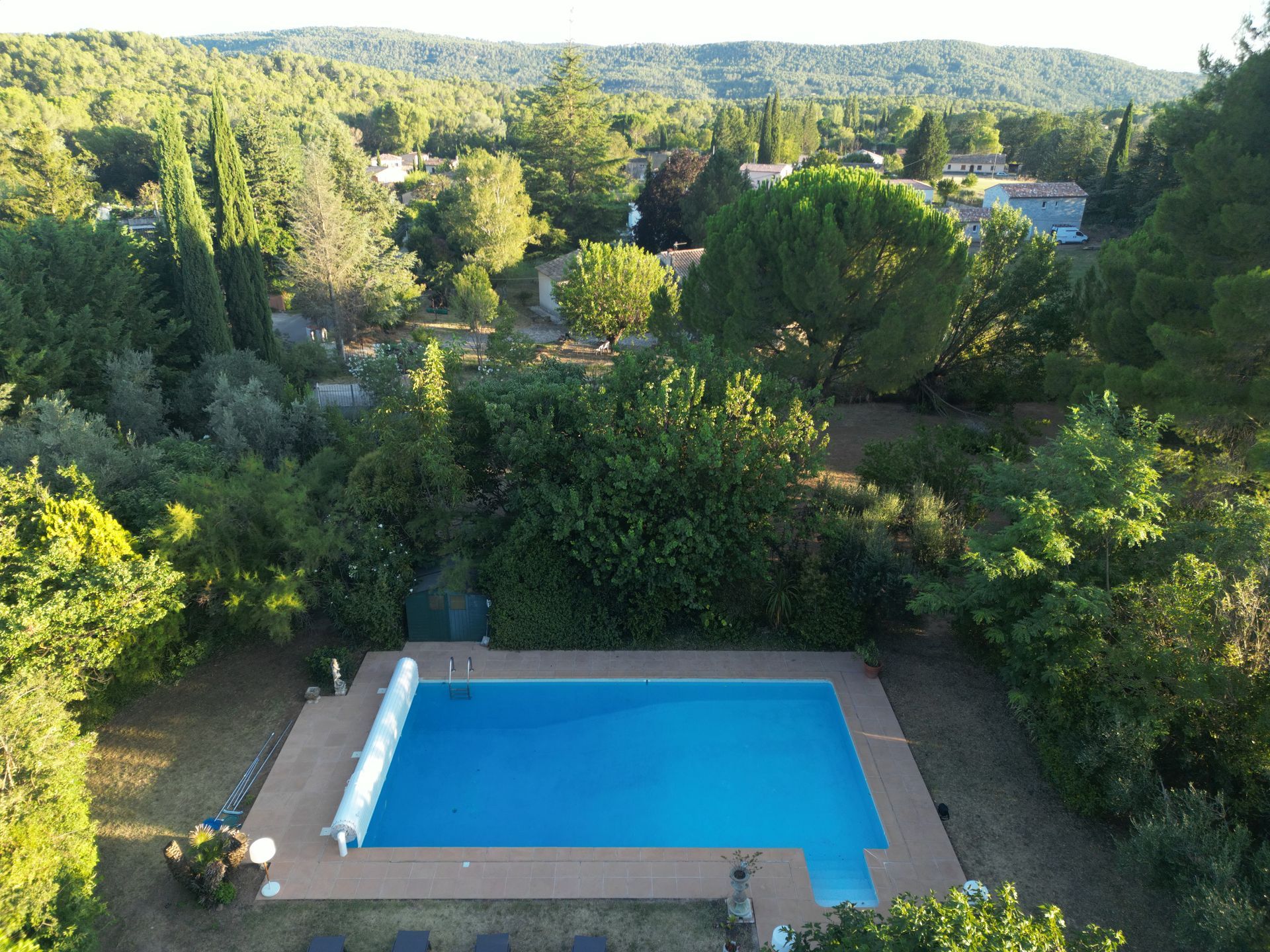 Piscine dans le jardin entourée d'une végétation luxuriante et de collines à l'horizon, vue d'en haut