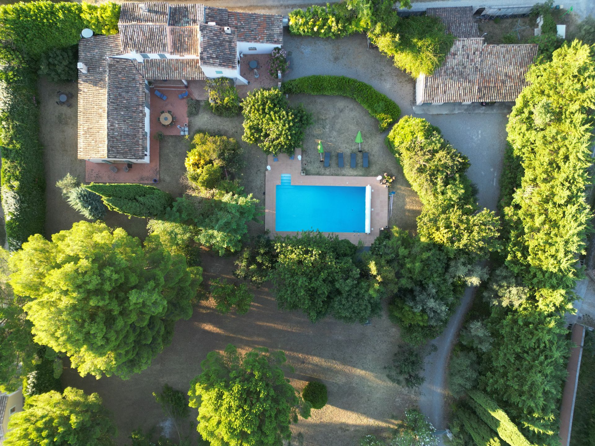 Vue aérienne d'une maison avec une piscine centrale, entourée d'arbres et d'allées de jardin.