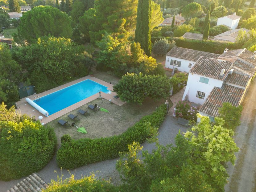 Vue aérienne d'une villa avec une piscine, un jardin et des allées sinueuses entourées d'arbres.
