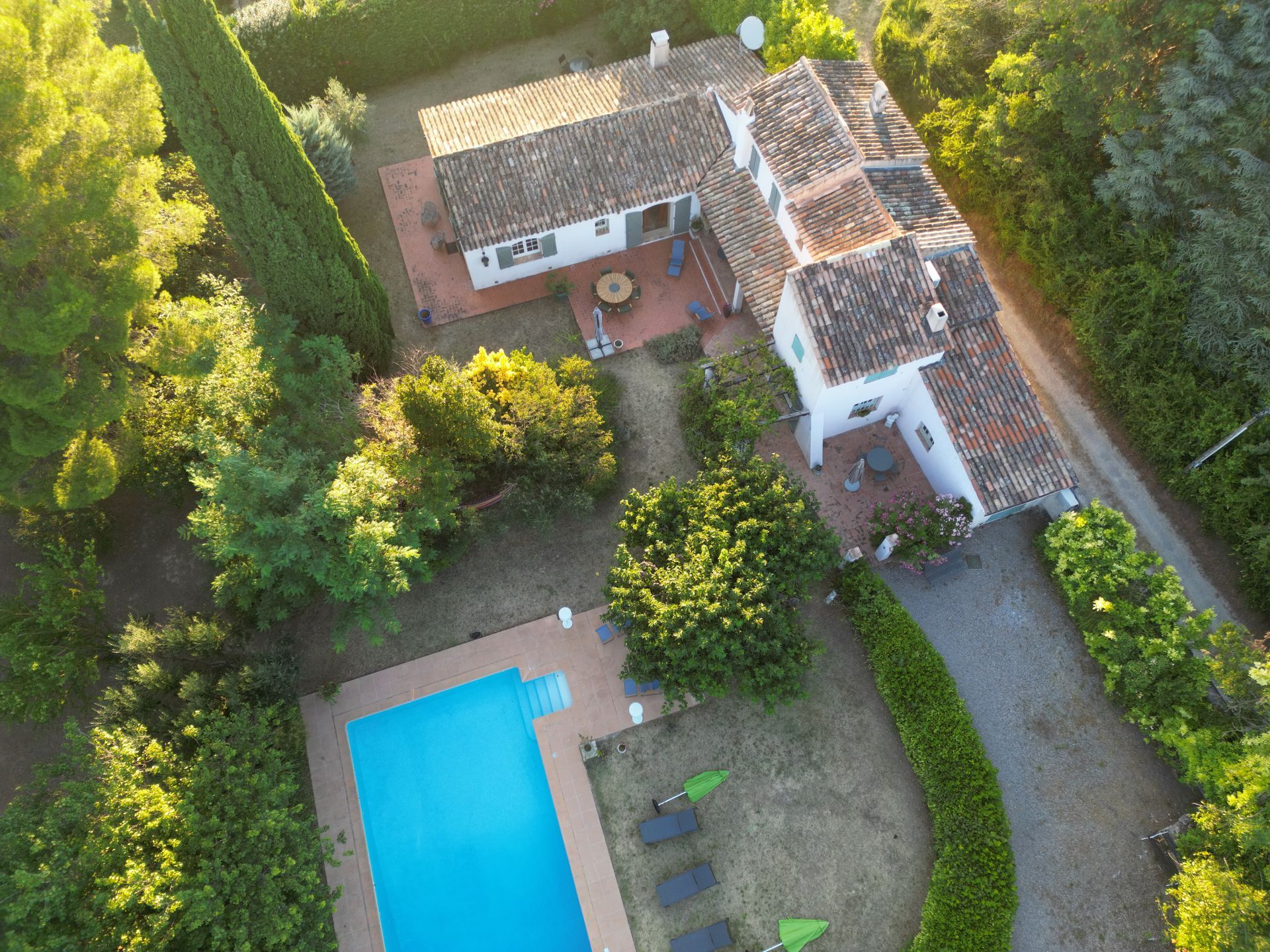 Vue aérienne d'une maison avec une piscine, une terrasse et des arbres environnants.