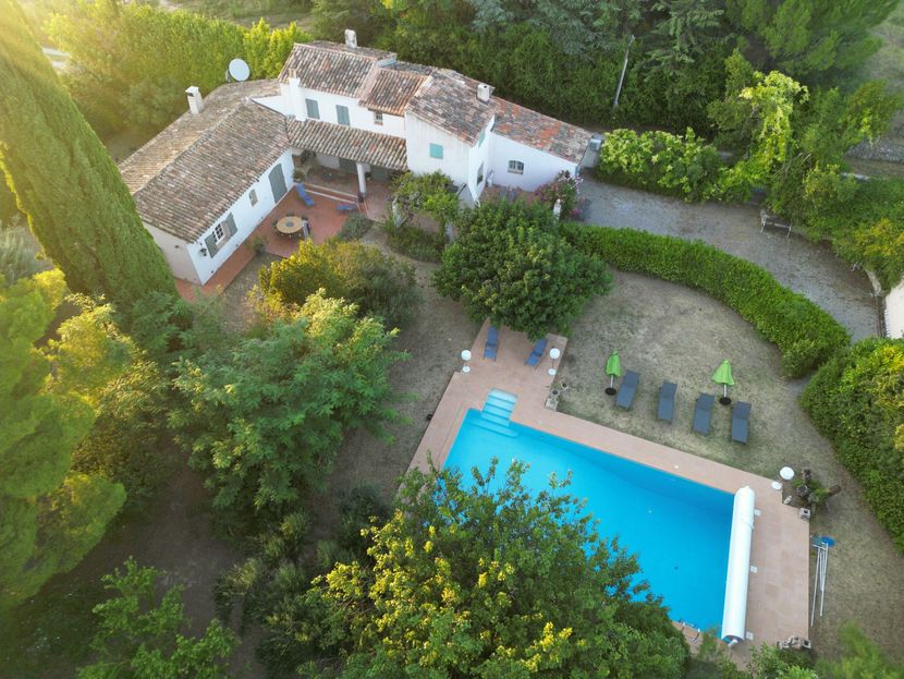 Vue aérienne d'une villa avec une piscine, des chaises longues sur la terrasse et une végétation luxuriante.