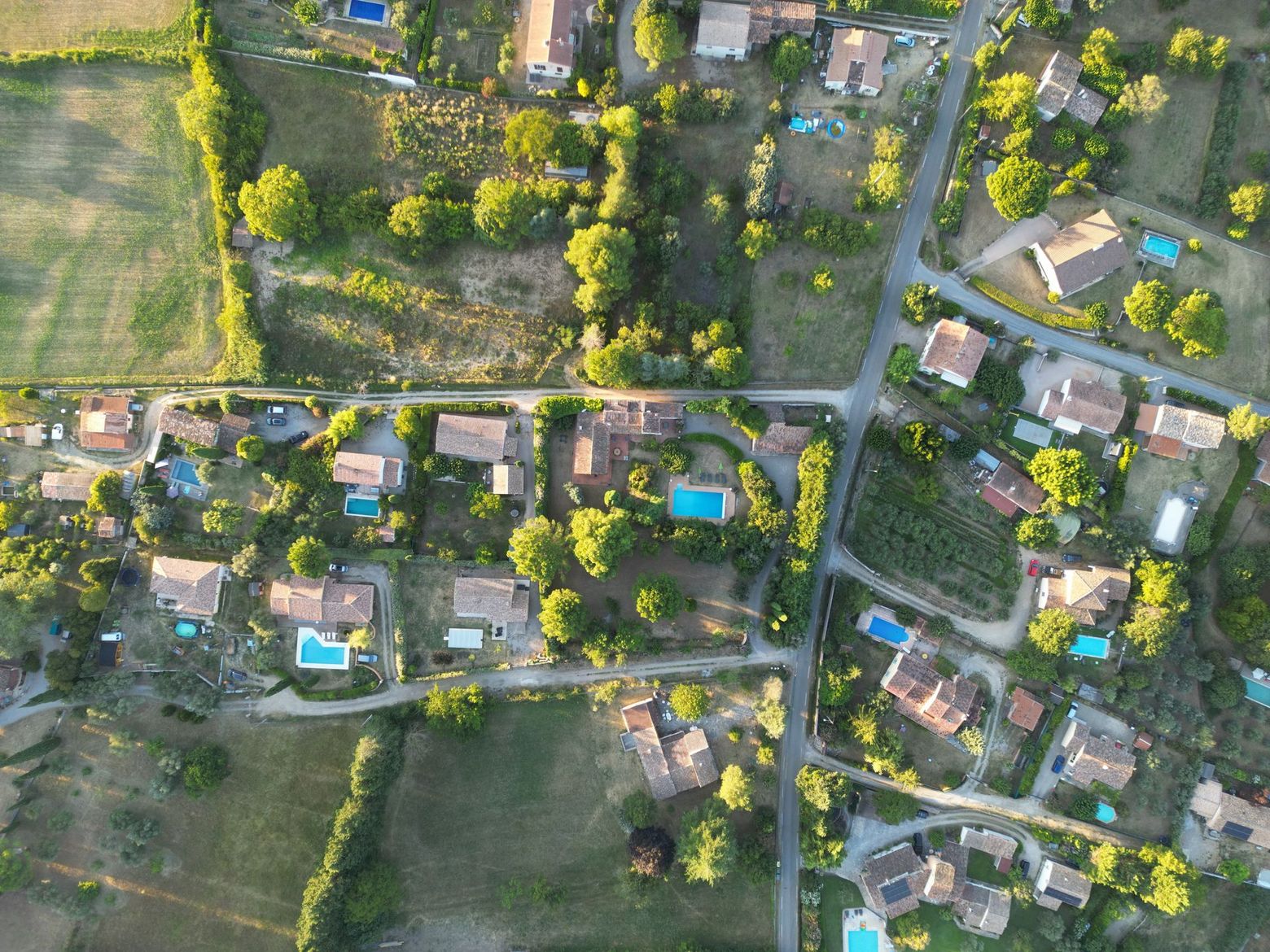 Vue aérienne d'un quartier rural avec des maisons éparses, des routes, des arbres et des piscines.
