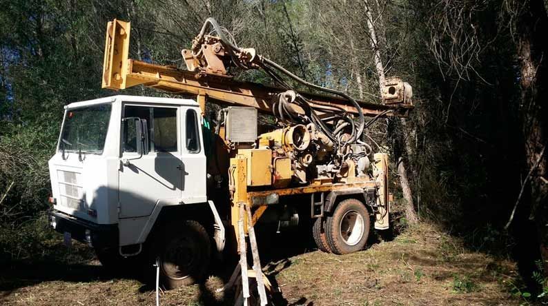 Un camión con un taladro acoplado está estacionado en medio de un bosque.