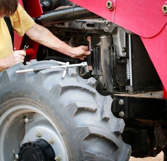 Un hombre está trabajando en un tractor rojo con una llave inglesa.