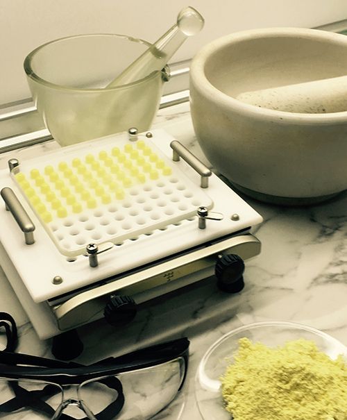 Herramientas de farmacia con llenadora de cápsulas y polvo sobre un mostrador.