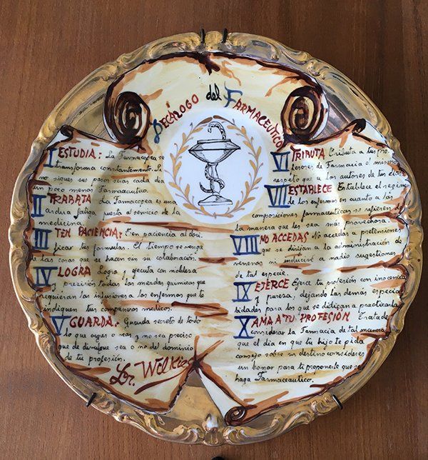 Plato decorativo con texto, símbolo farmacéutico y elementos de pergamino; borde dorado.