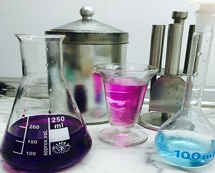 Cristalería de laboratorio con líquidos de color violeta y azul.