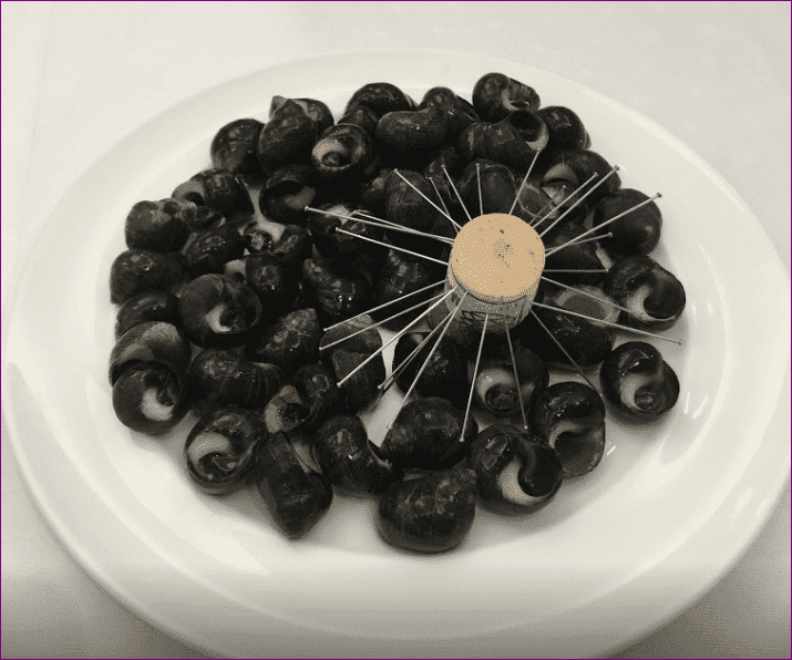 Un plato blanco cubierto con aceitunas negras y un molinillo de madera.