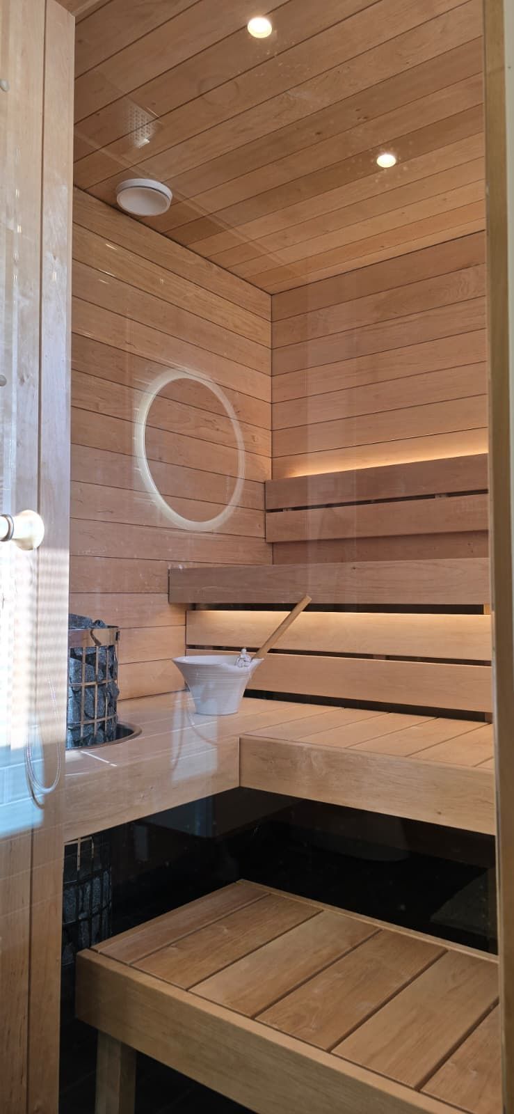 Puupaneloitu sauna, jossa on lauteet, pyöreä peili ja lämmin upotettu valaistus