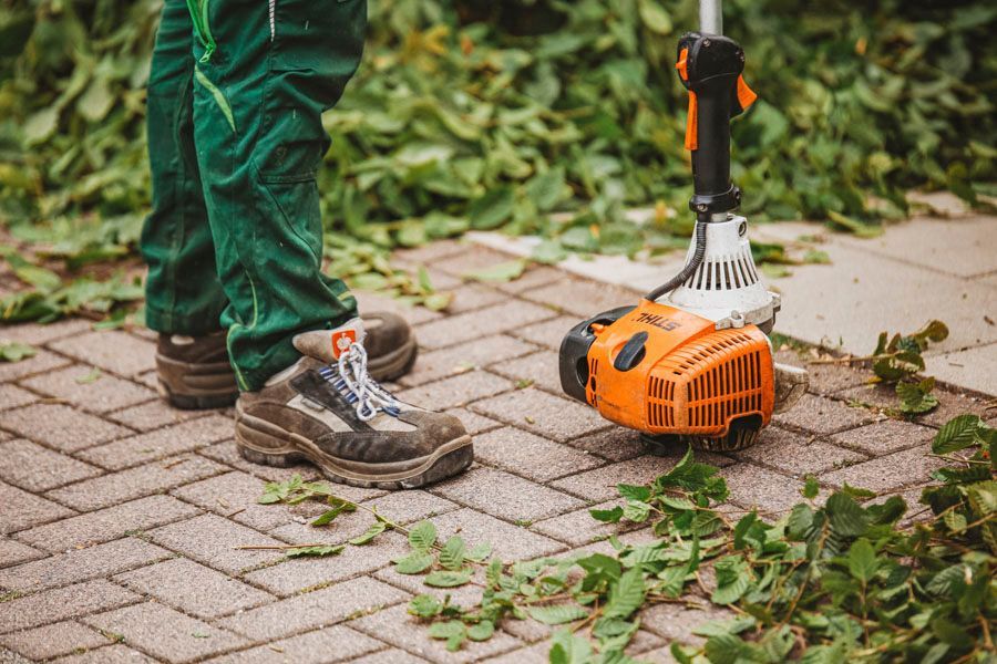 Eine Person benutzt einen Rasenmäher auf einem Gehweg aus Ziegeln.