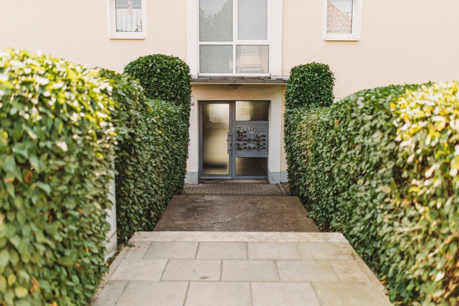 Ein von Büschen umgebener Gehweg, der zur Eingangstür eines Gebäudes führt.