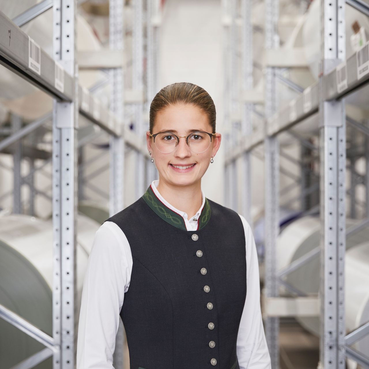 Eine Frau mit Brille und schwarzer Weste steht in einer Lagerhalle