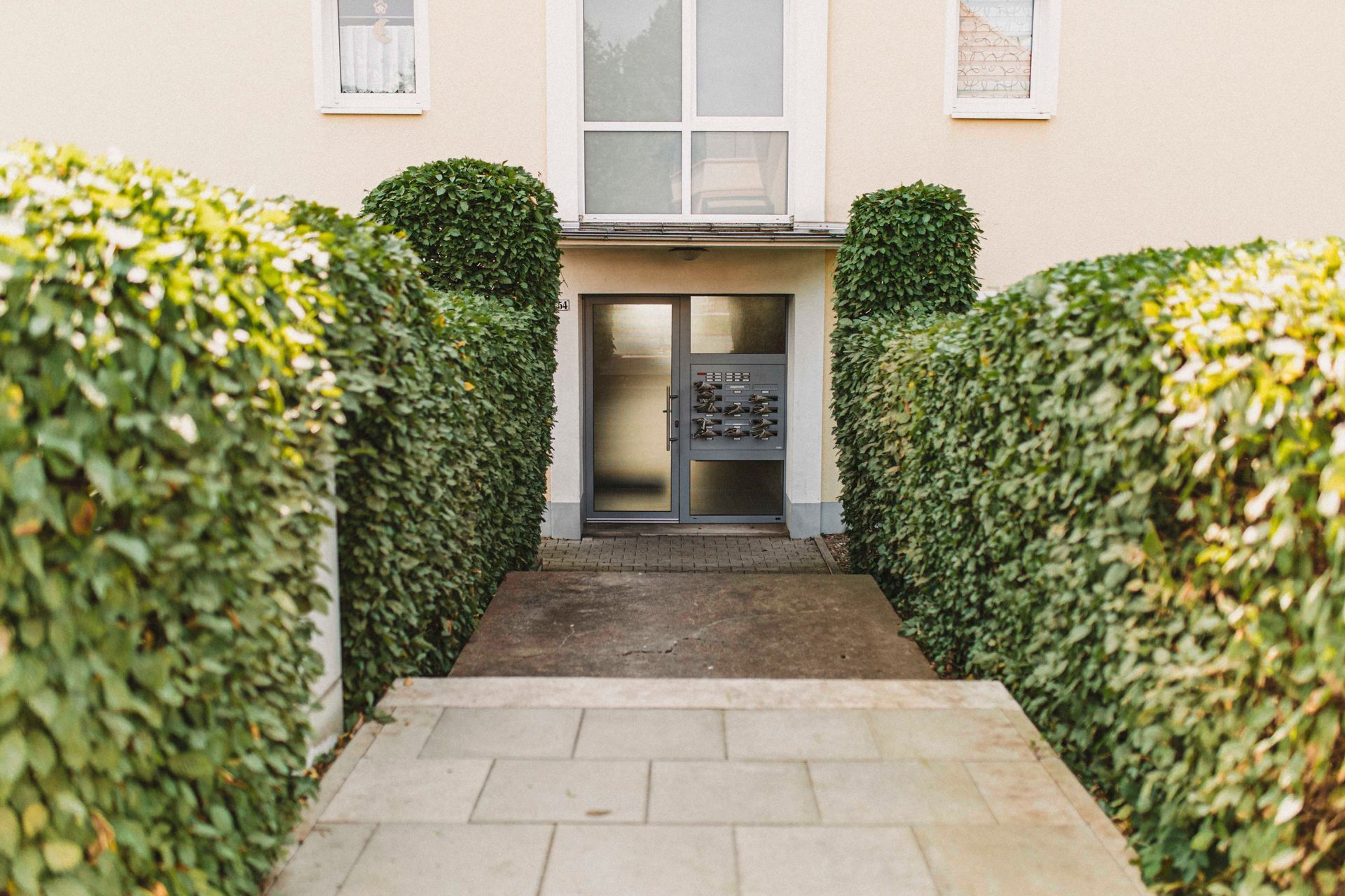 Ein von Büschen umgebener Gehweg, der zum Eingang eines Gebäudes führt.
