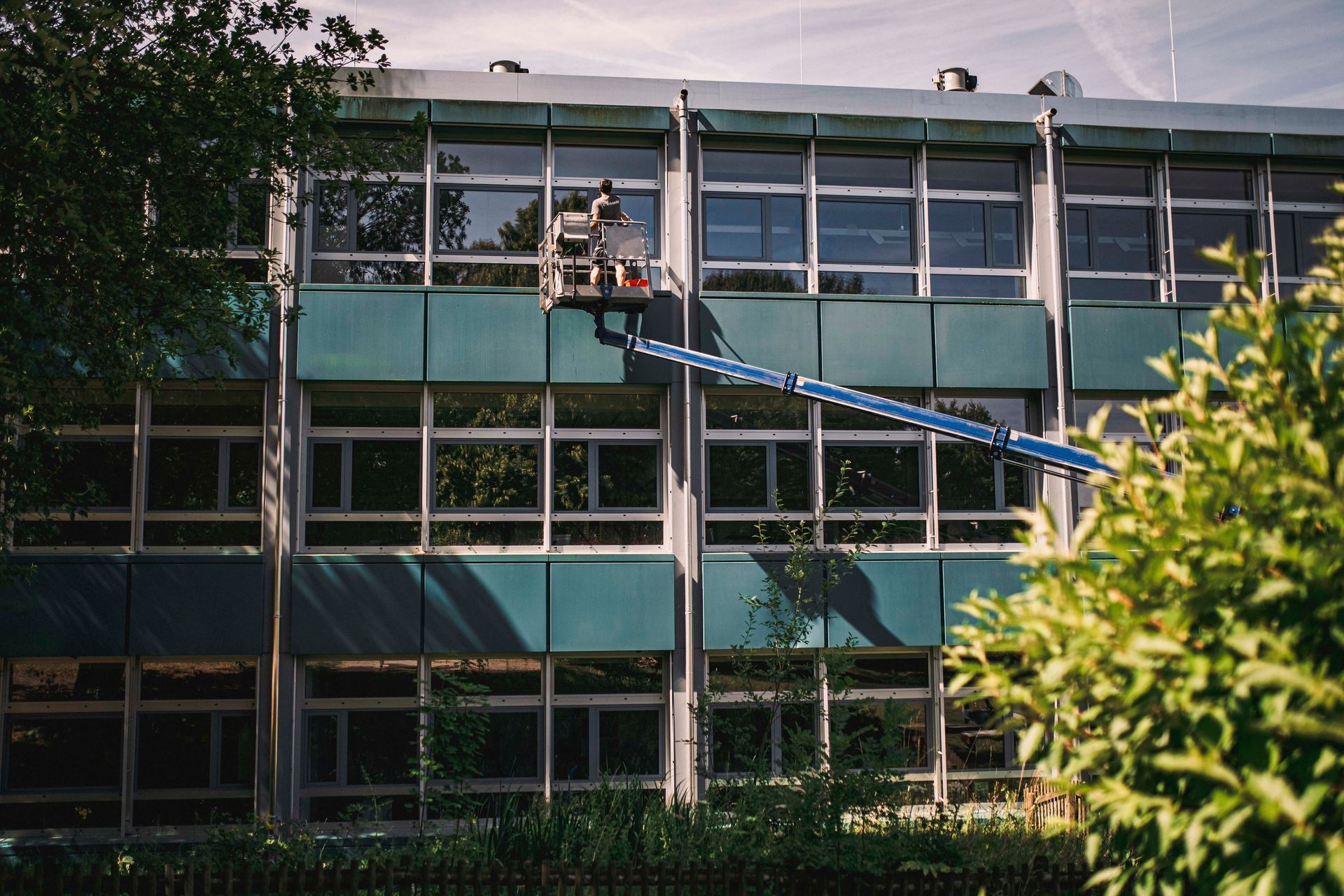 Ein Mann reinigt mit einem Kran die Fenster eines Gebäudes.