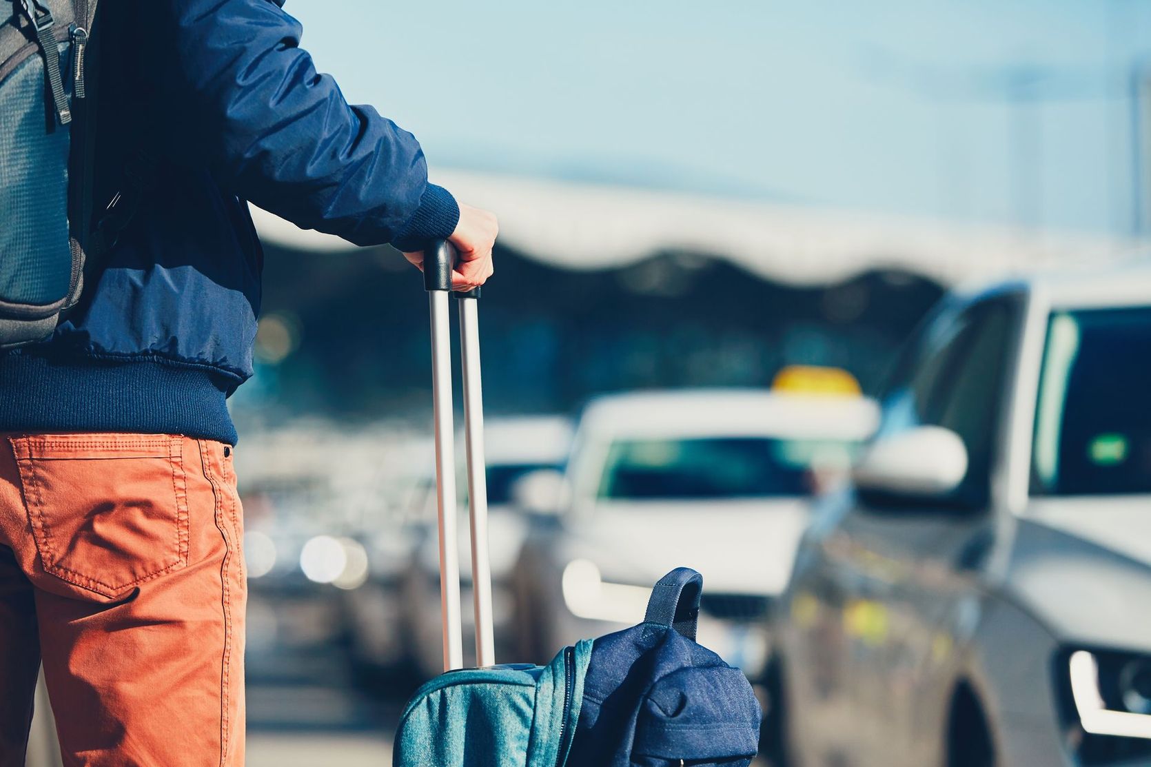 Voyageur avec valise à roulettes et sac à dos traversant un parking très fréquenté