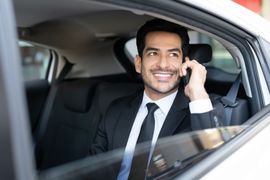 Un homme en costume sourit en parlant au téléphone dans une voiture