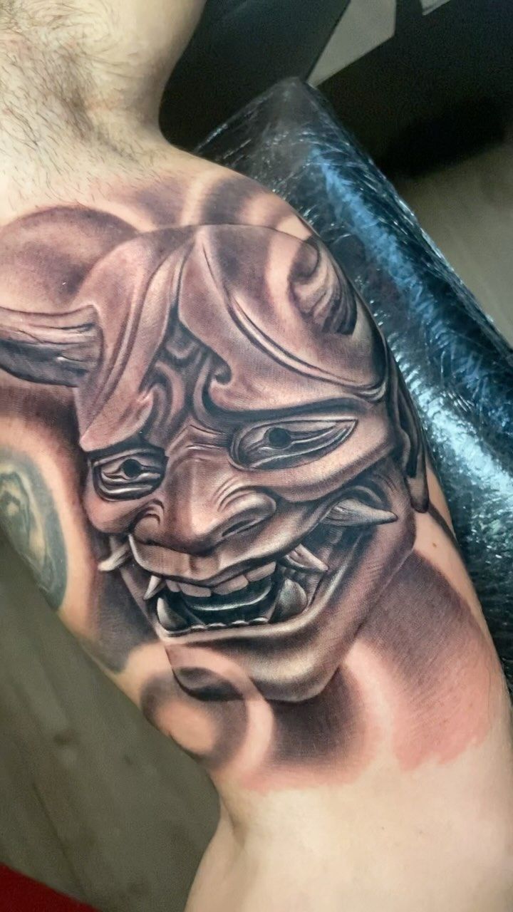 Un hombre tiene un tatuaje de una máscara de demonio en su hombro.