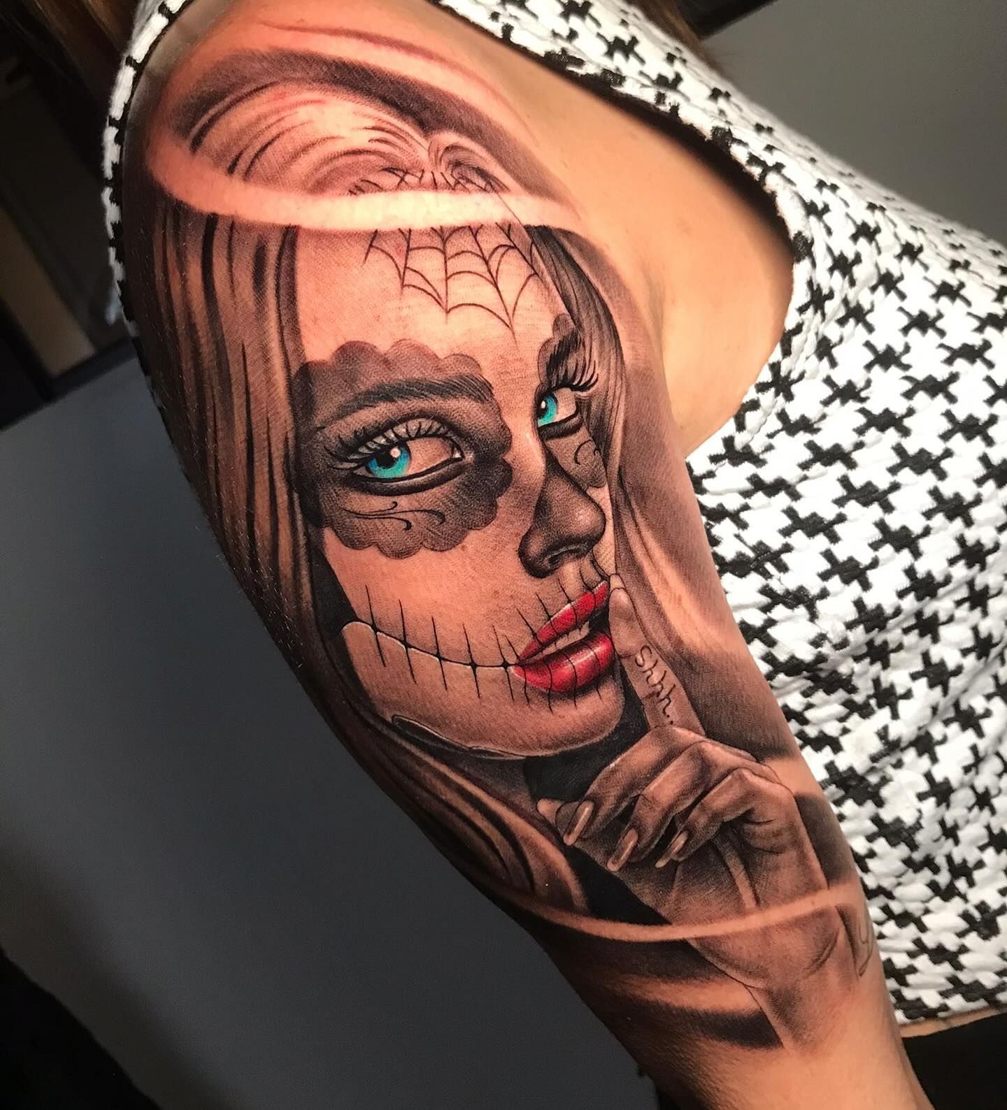 Tatuaje de una mujer con diseño de calavera de azúcar, ojos azules, labios rojos y un gesto de 