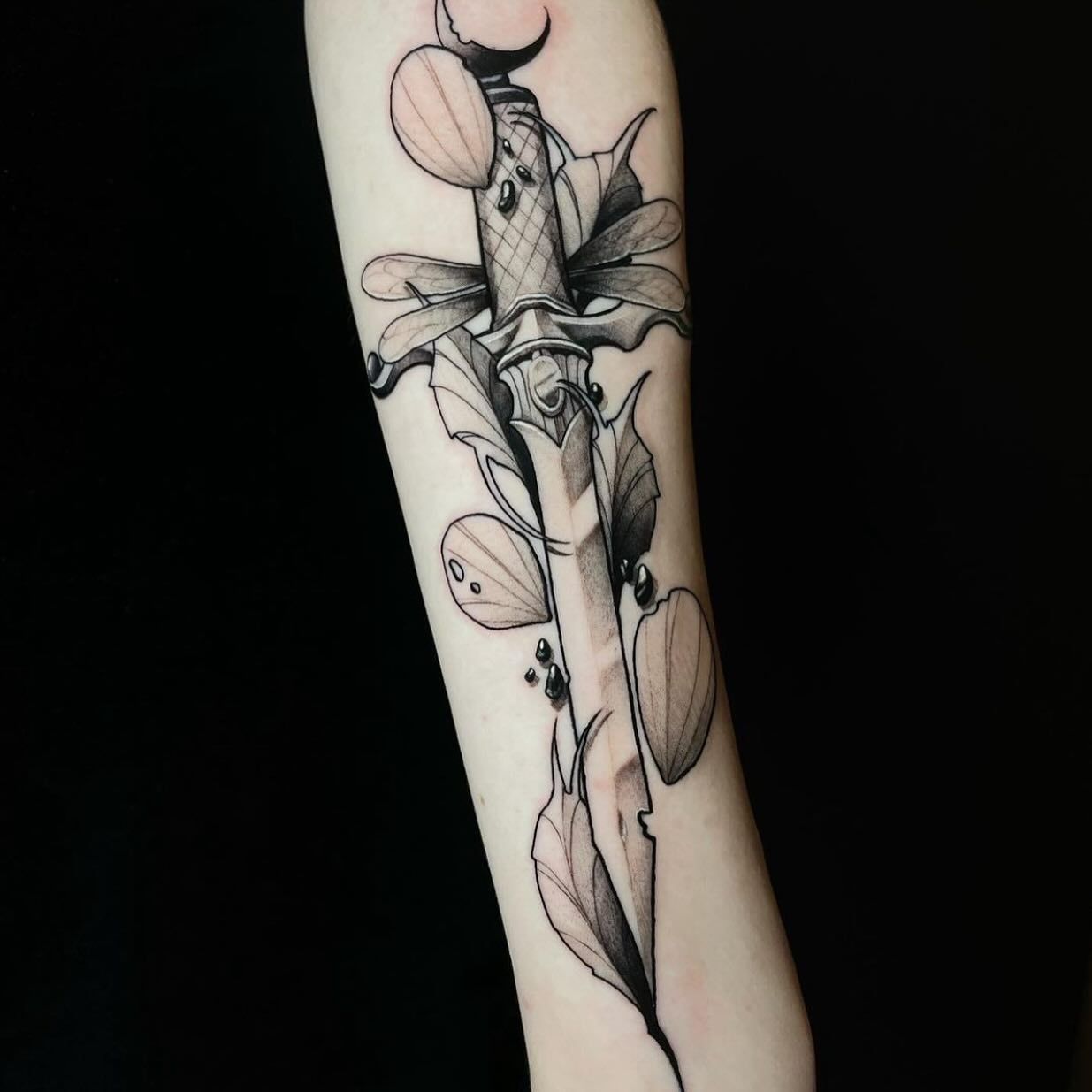 Una persona tiene un tatuaje de una daga con flores.