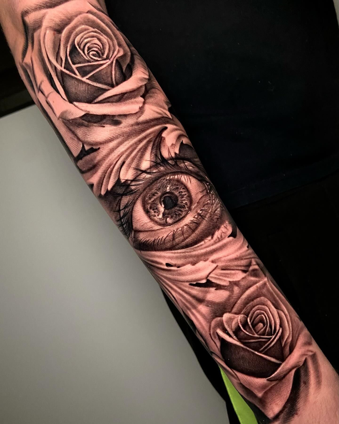 Un tatuaje en blanco y negro de un ojo y rosas en un antebrazo.