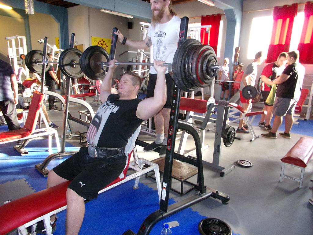 Plusieurs personnes utilisant les machines de la salle de musculation, dont un homme au premier plan se servant des haltères