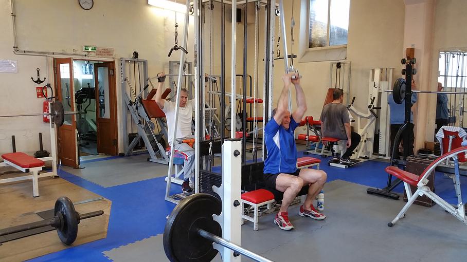 Machine de musculation au centre utilisée par deux hommes pour travailler les bras et le dos
