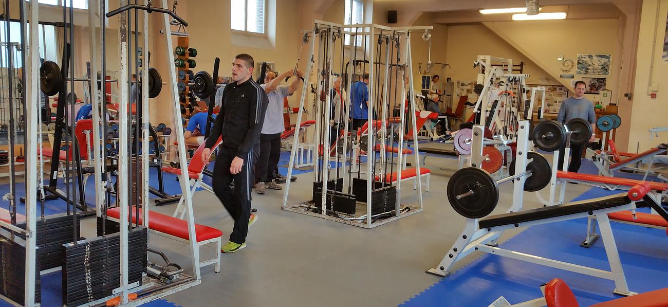 Salle de sport munie de plusieurs équipements de musculation et occupée par plusieurs utilisateurs