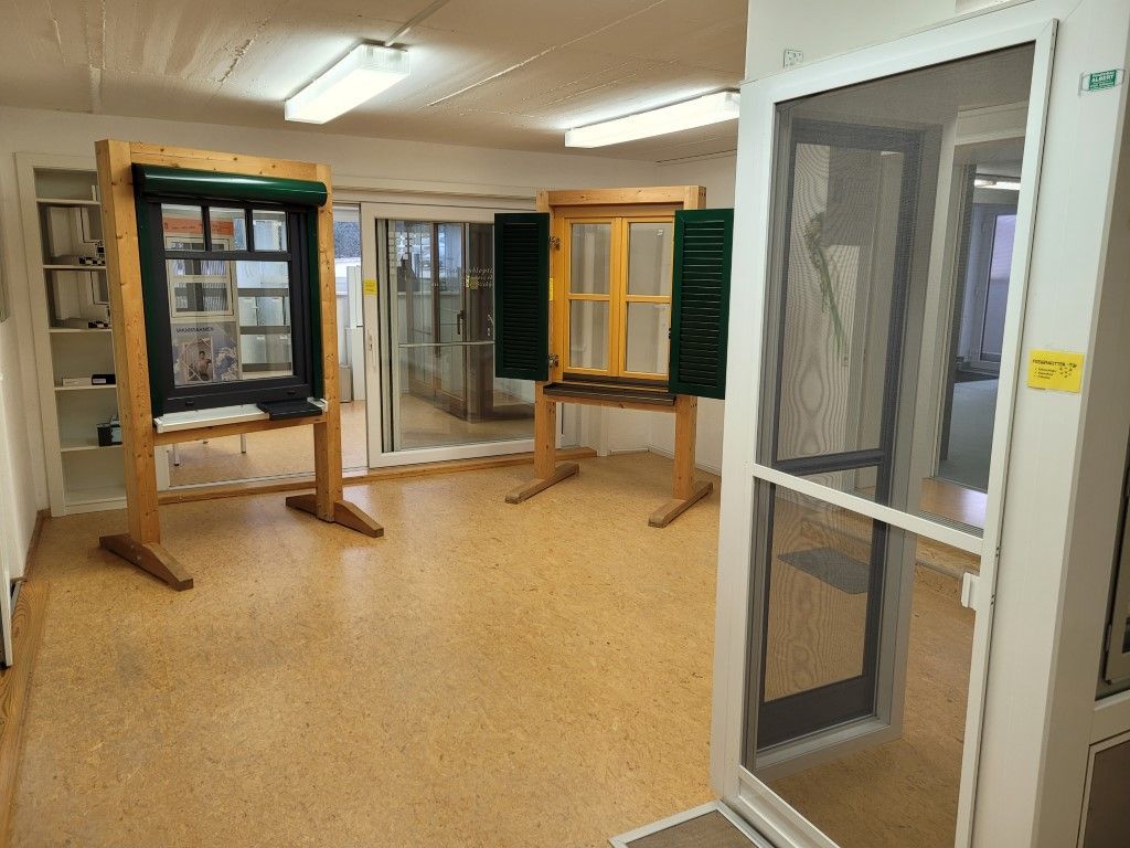 Showroom mit Schaufenster- und Türdisplays auf Holzständern; heller Boden, weiße Wände.