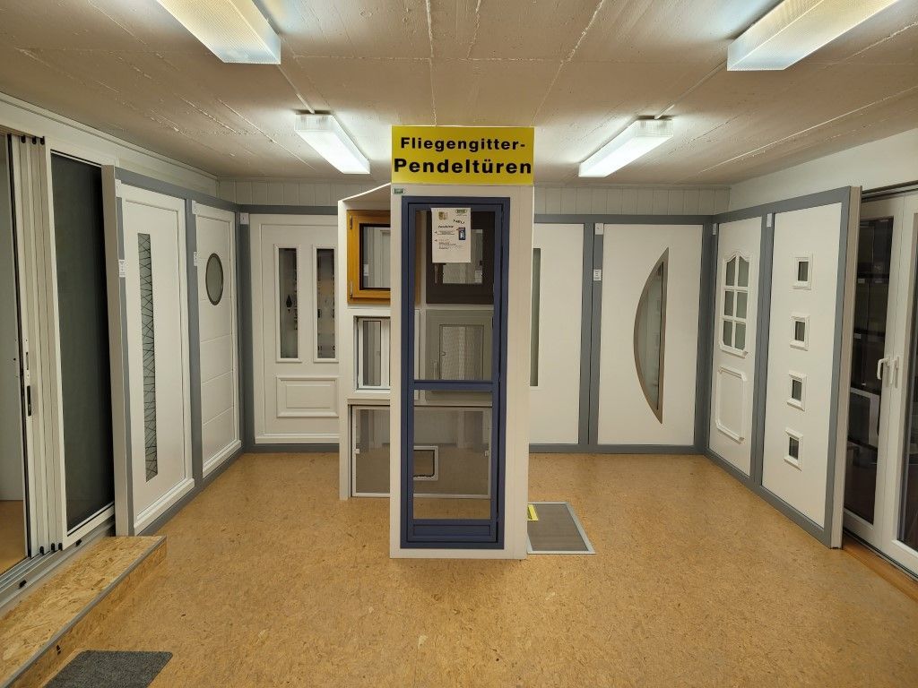 Ein Ausstellungsraum mit verschiedenen Türstilen; weiß, einige mit Fenstern, auf einem Holzboden, unter hellem Licht.