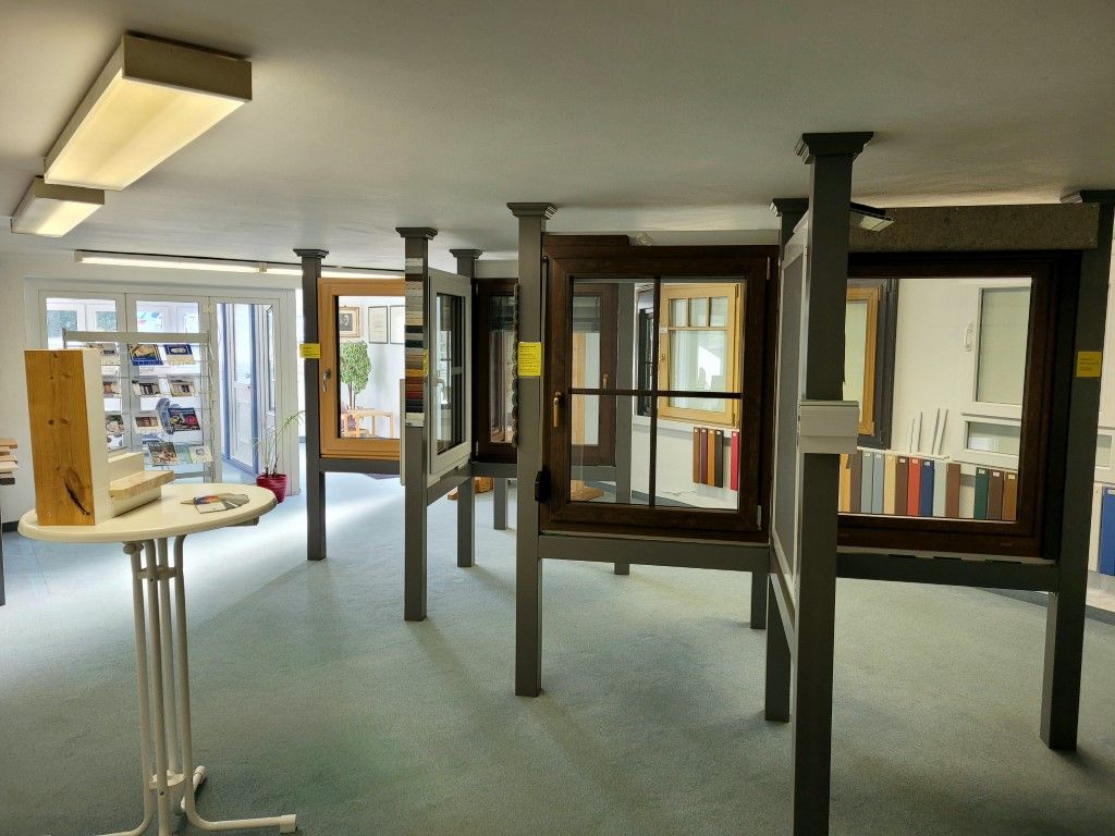 Ein Ausstellungsraum mit verschiedenen Schaufenstern auf Ständen. Hellblauer Teppich, weiße Wände und Leuchtstoffröhrenbeleuchtung.