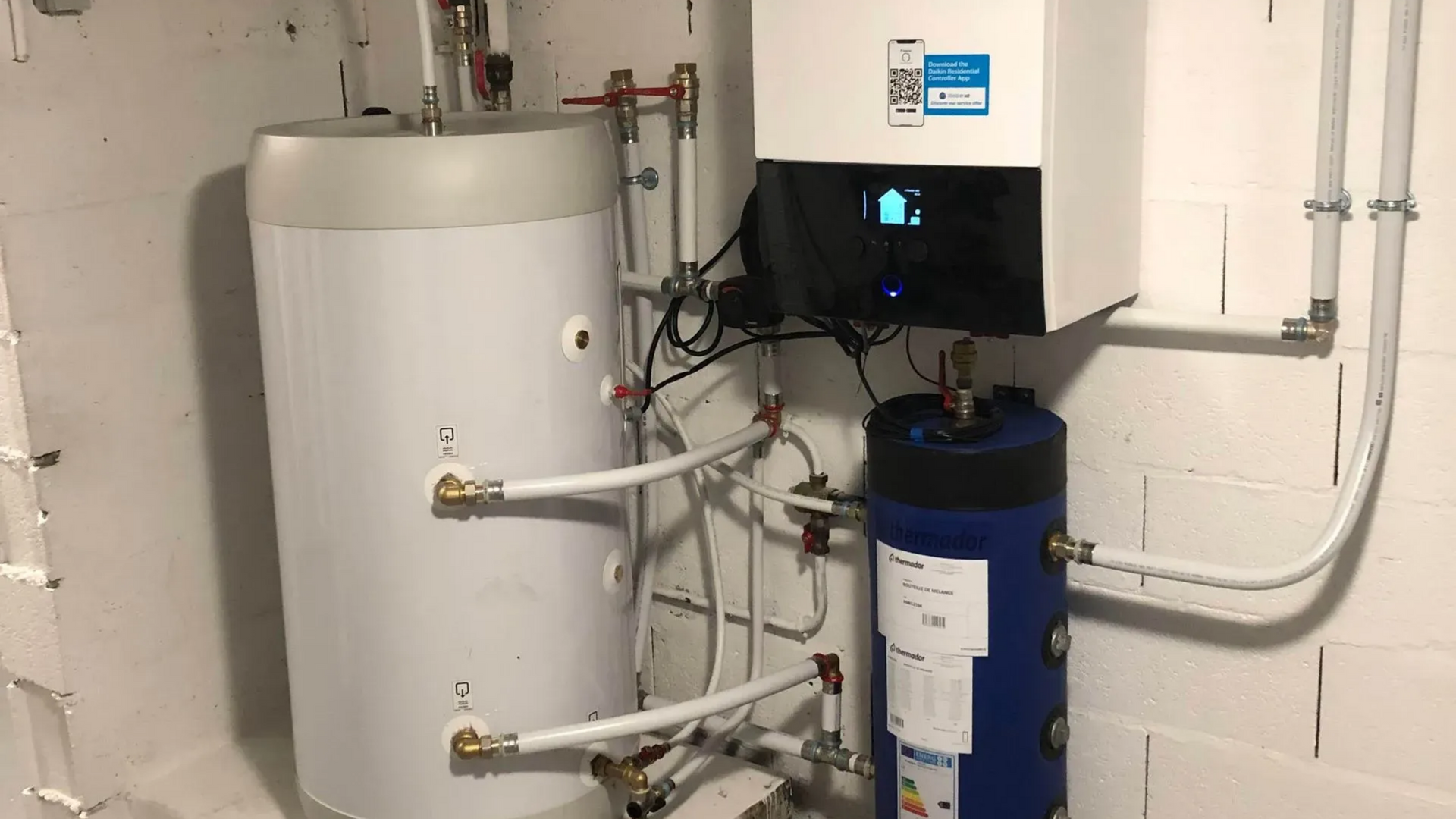 Système de chauffage d'eau blanc et bleu contre un mur de briques blanches. Réservoirs cylindriques, tuyaux et panneau de commande.