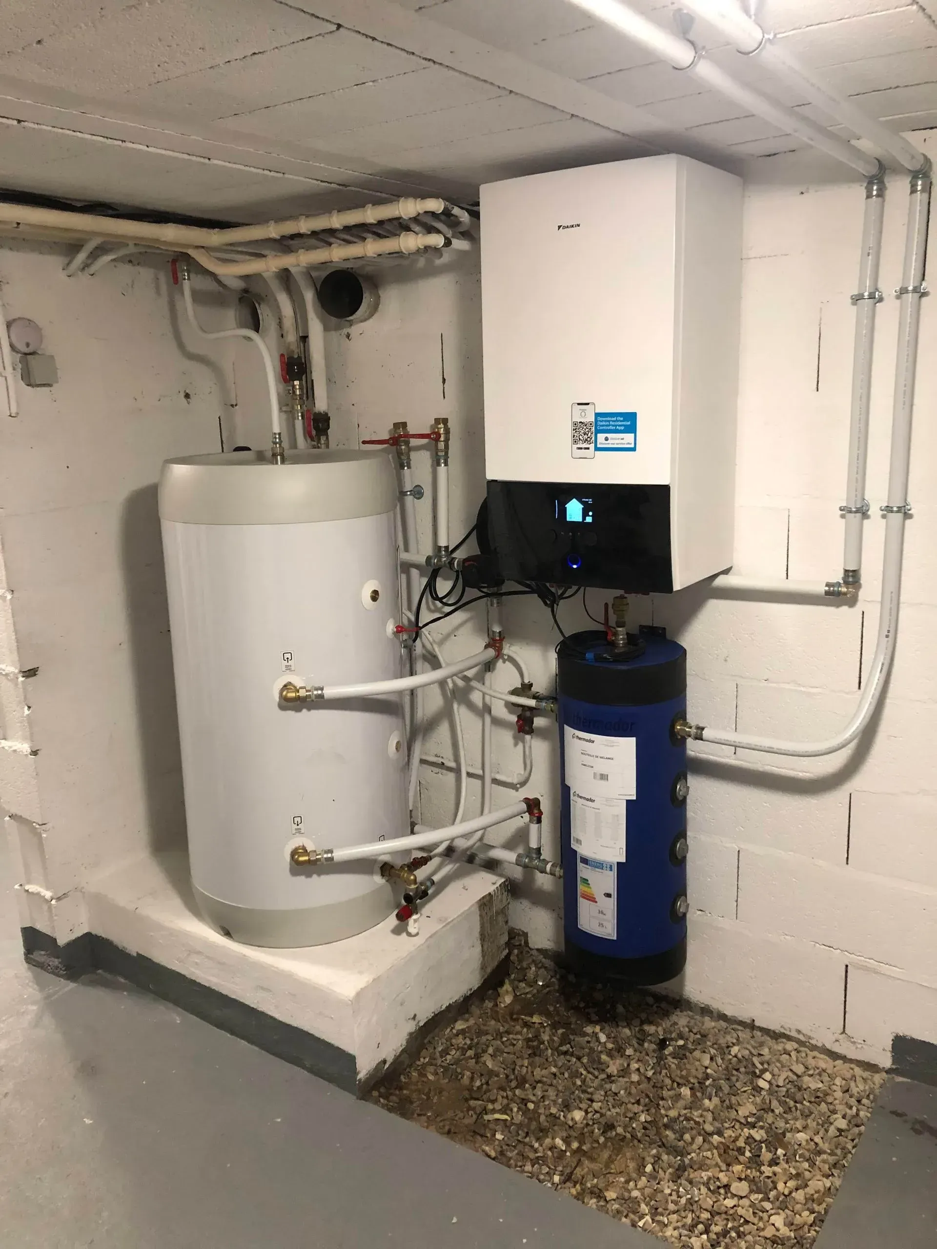 Système de chauffage dans un sous-sol comprenant une unité murale blanche, un réservoir d'eau et un filtre à eau bleu.