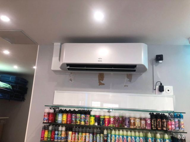 Unité de climatisation blanche fixée au mur au-dessus d'étagères remplies de flacons de liquide à vapoter colorés.