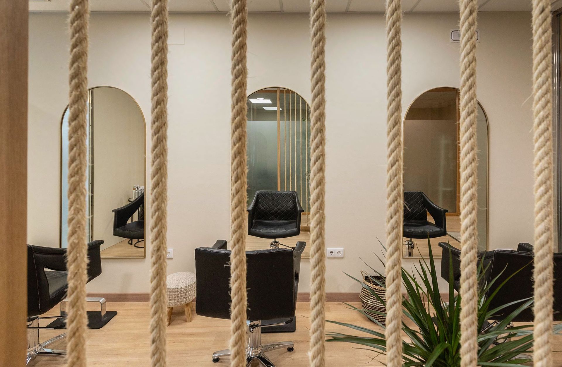 Interior de peluquería con espejos en forma de arco, sillas negras y detalles de cuerda natural.