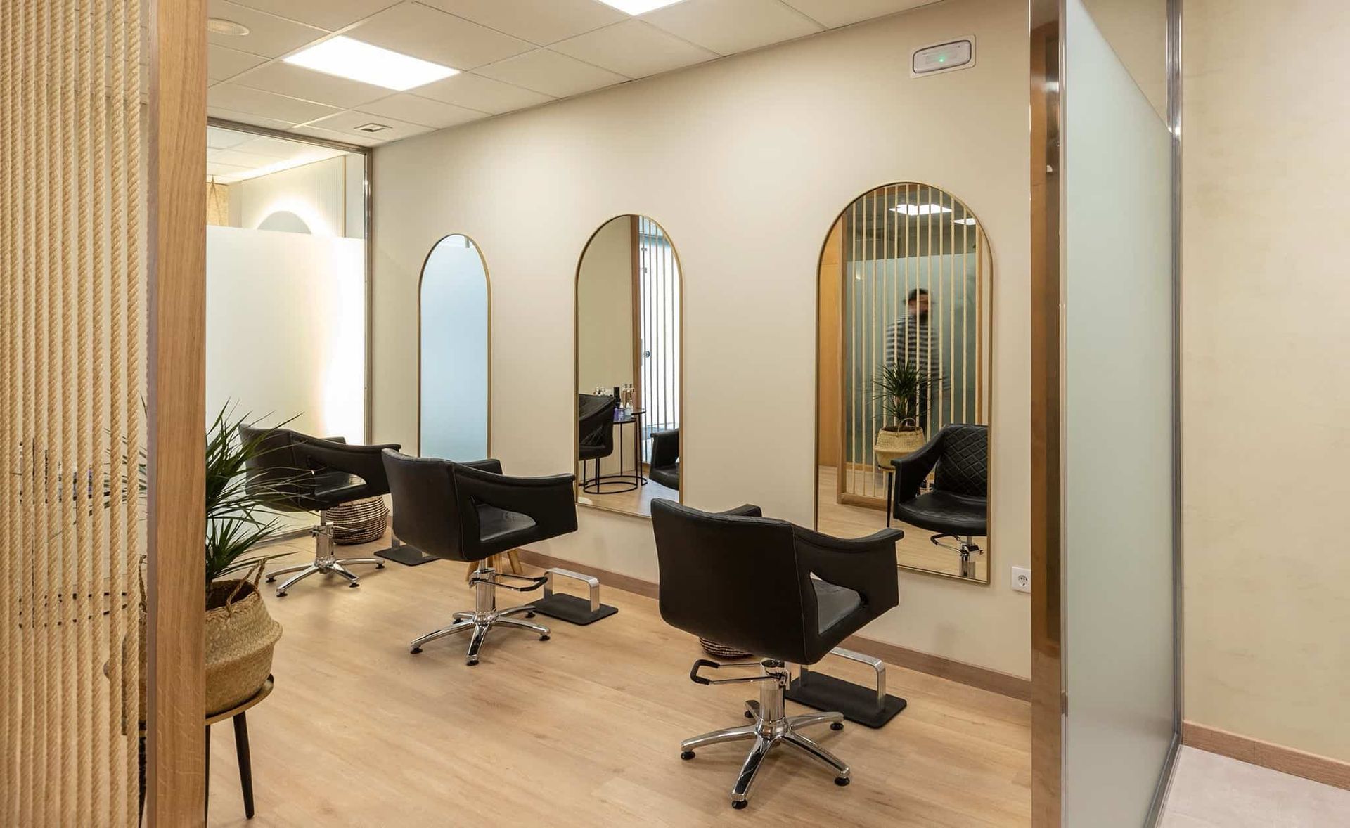 Interior de peluquería con espejos, sillas y una persona reflejada en uno de ellos.