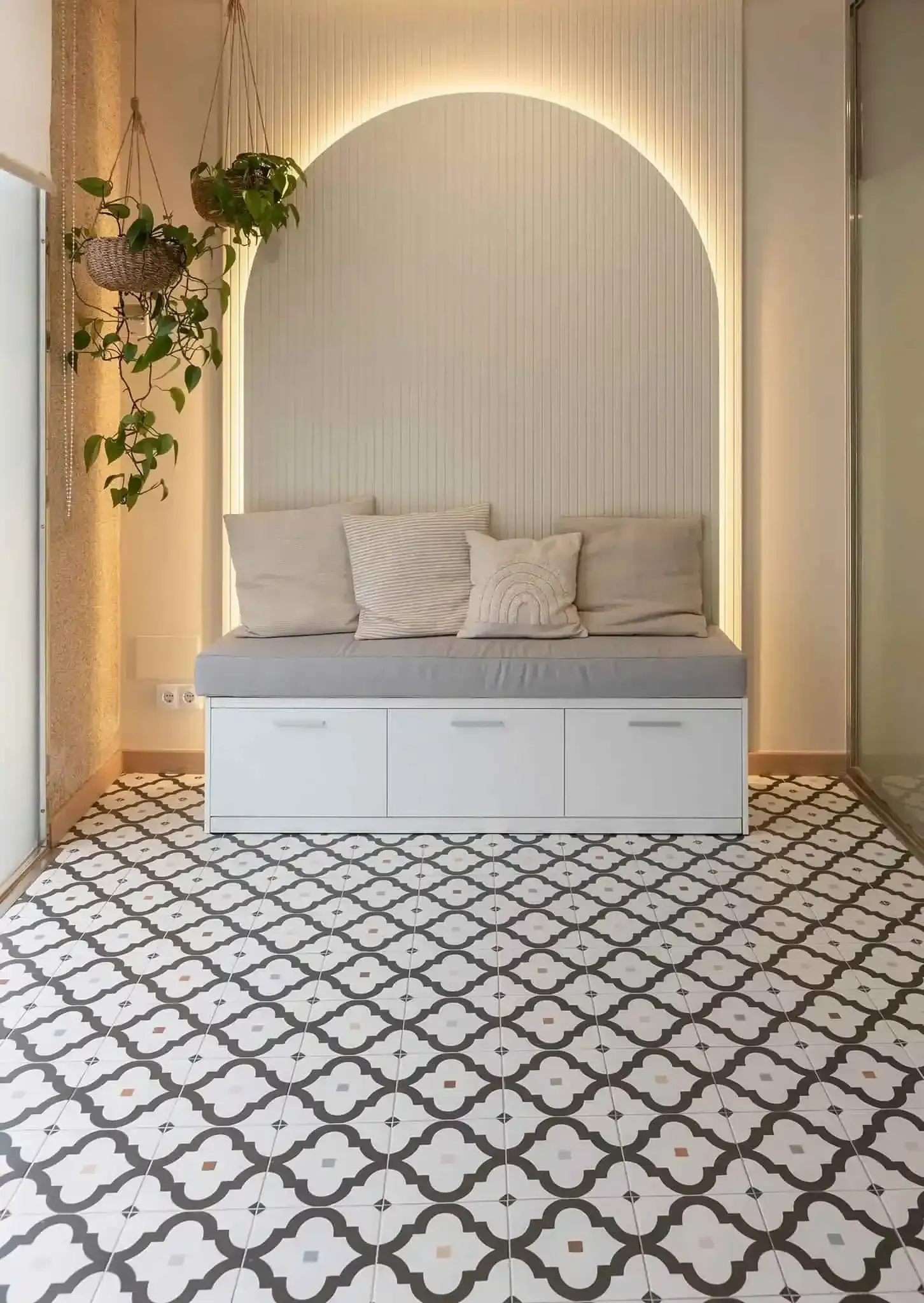 Acogedora zona de estar blanca con pared arqueada, almohadas, plantas y suelo estampado.