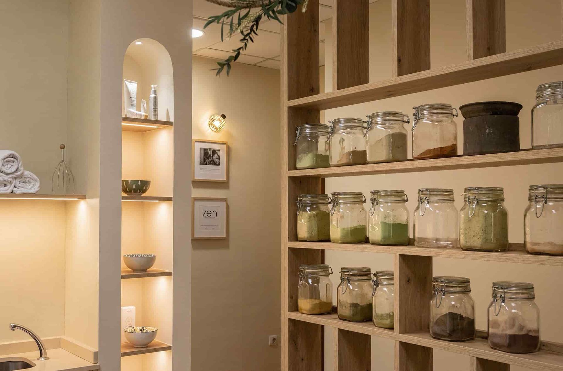 Estantes con frascos de ingredientes en un spa. Paredes beige, estanterías de madera y un rincón iluminado.