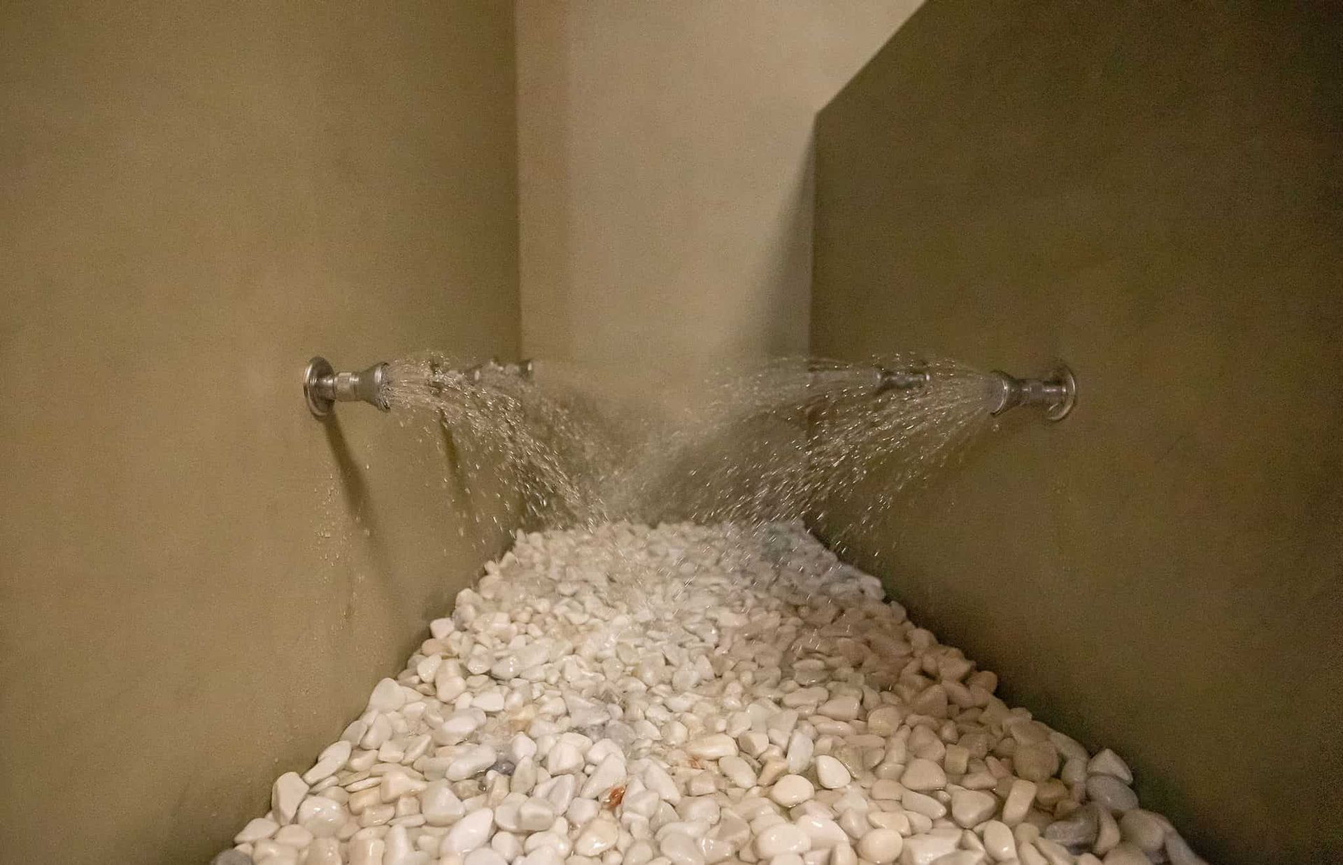 Ducha con agua en cascada sobre un lecho de piedras blancas de río en un rincón.