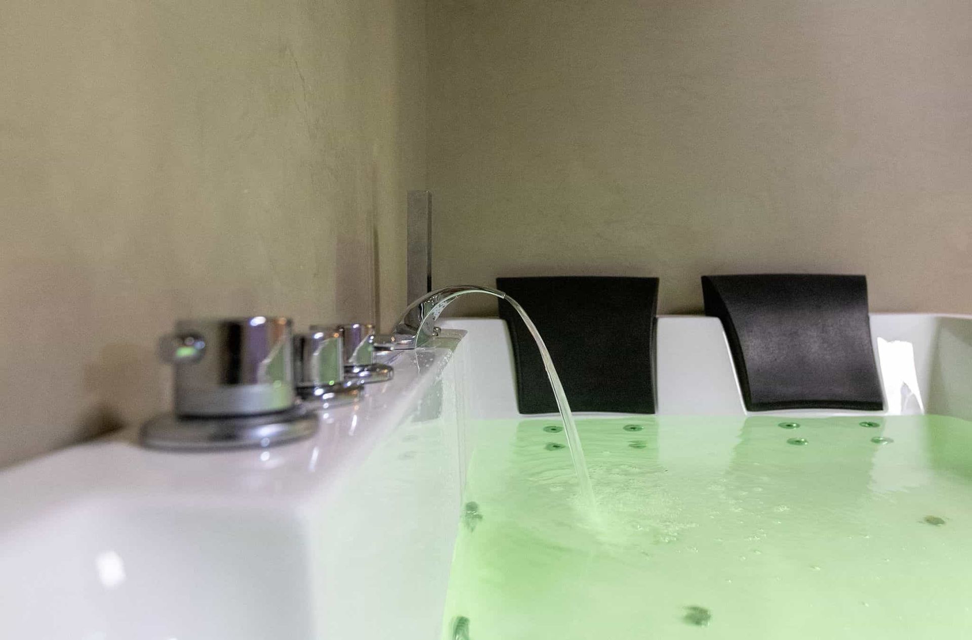 Una bañera moderna con grifería cromada, agua corriente y reposacabezas negros. Se ve agua teñida de verde.