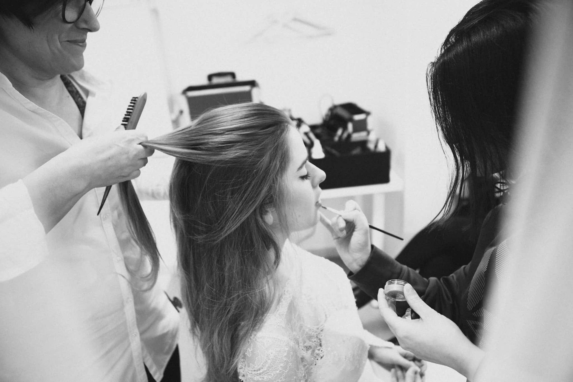 Una mujer recibe el peinado y el maquillaje de dos personas en una habitación luminosa.