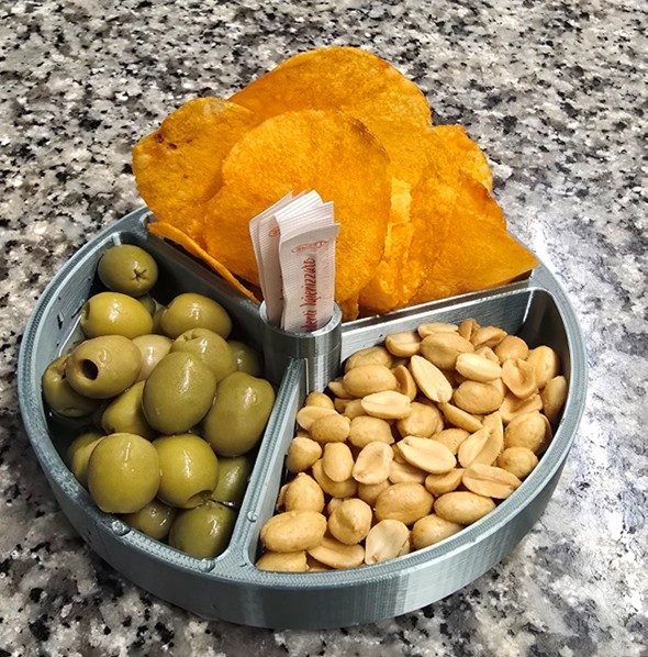 Vassoio rotondo per snack con olive verdi, arachidi e patatine arancioni su un piano di lavoro