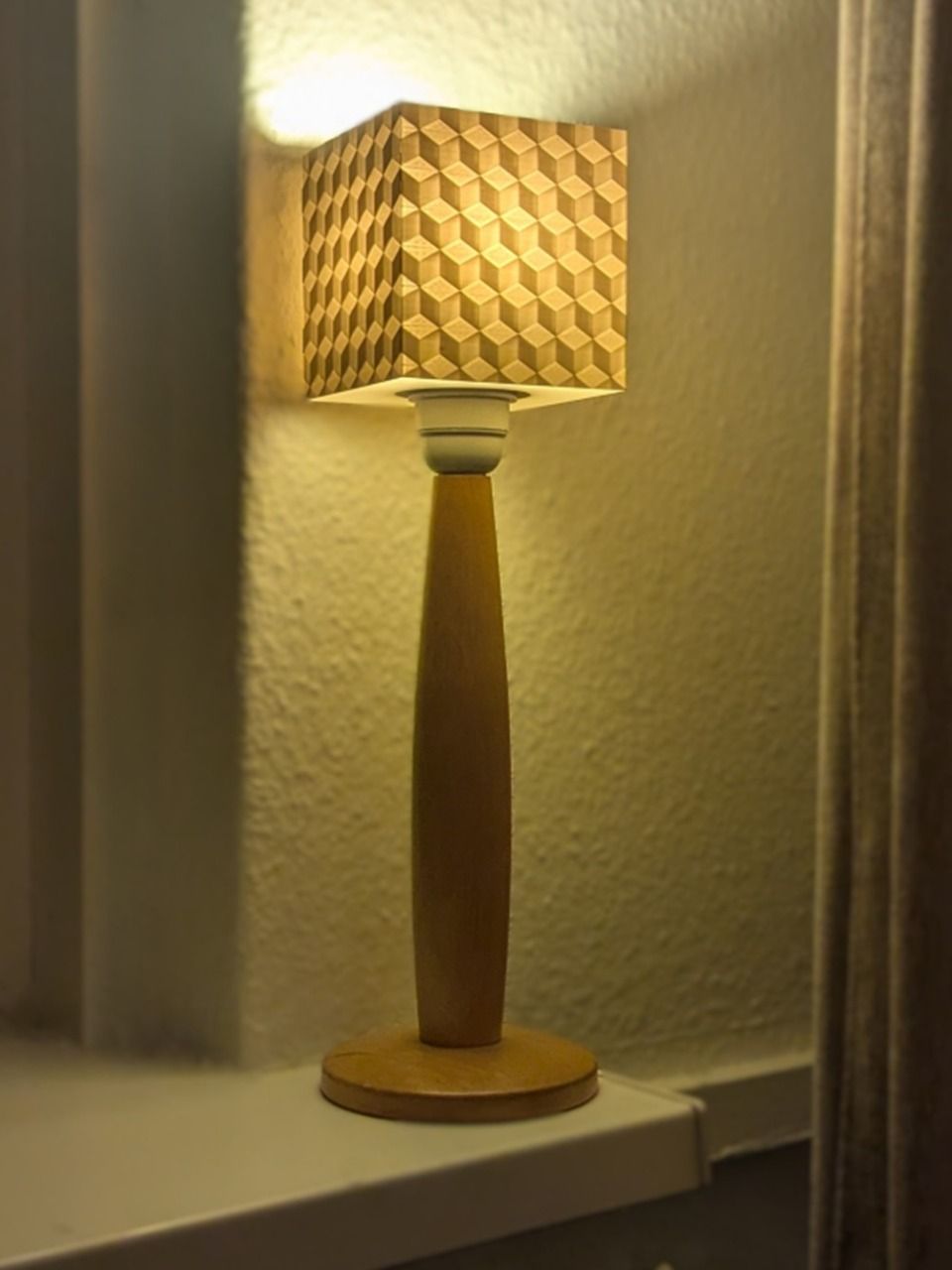 Lampada da tavolo con base in legno e paralume decorato, che illumina una nicchia angolare.